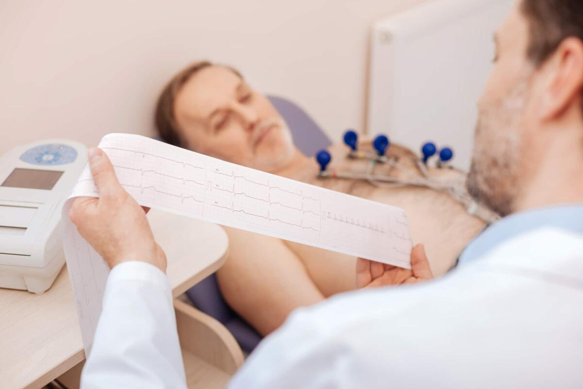 Un nuovo algoritmo di Intelligenza Artificiale "batte" in precisione il classico cardiologo - Thorough study. Prominent precise attentive doctor holding a paper tape and reading graphical recording he just completed making with his patient