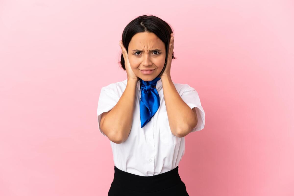 Perché ci si tappano le orecchie quando viaggiamo in aereo? - Airplane stewardess over isolated background frustrated and covering ears