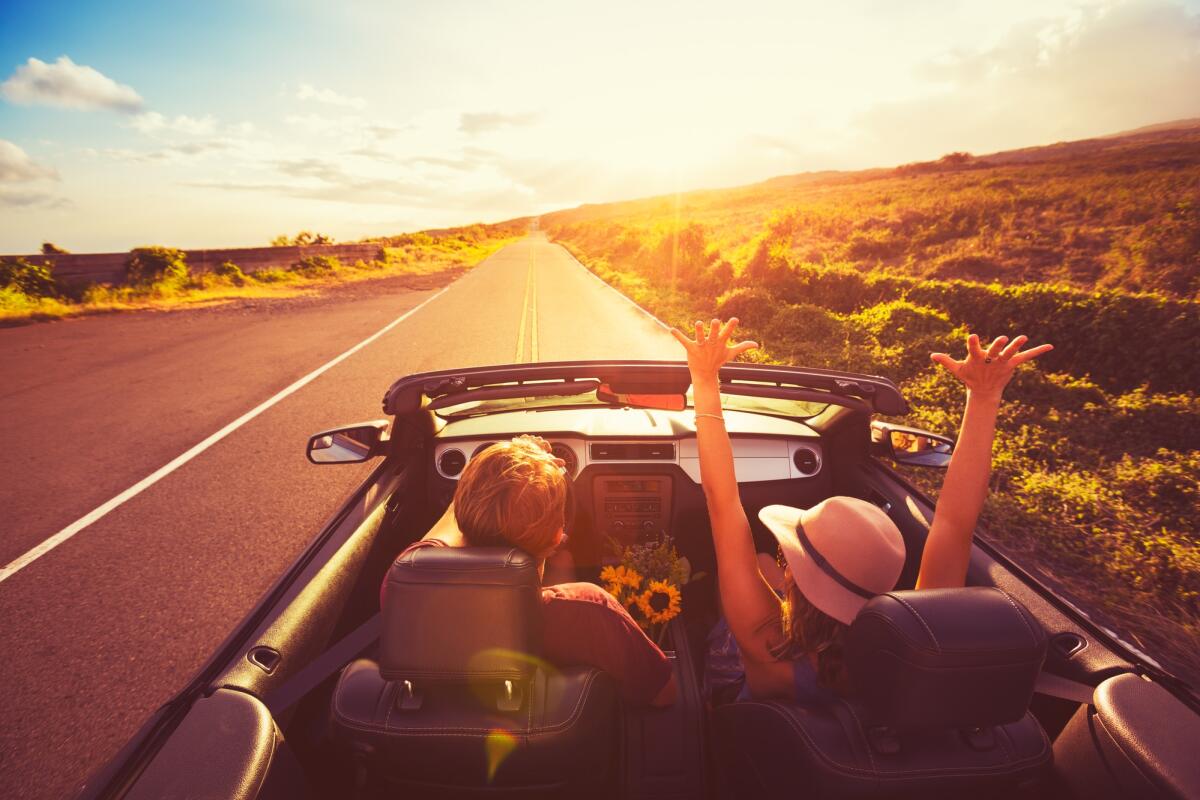 Partire per un viaggio in auto: tutto ciò che c’è da controllare - Happy Young Couple Driving Along Country Road in Convertable at Sunset. Freedom Adevnture Roadtrip!