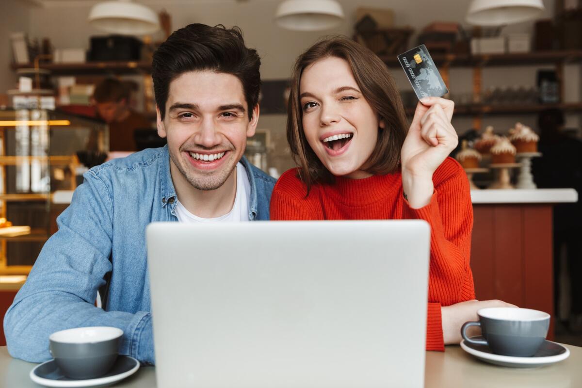 Quali fattori bisogna tenere in considerazione quando si apre un conto online - Excited young couple showing credit card and sitting at the cafe table with laptop computer