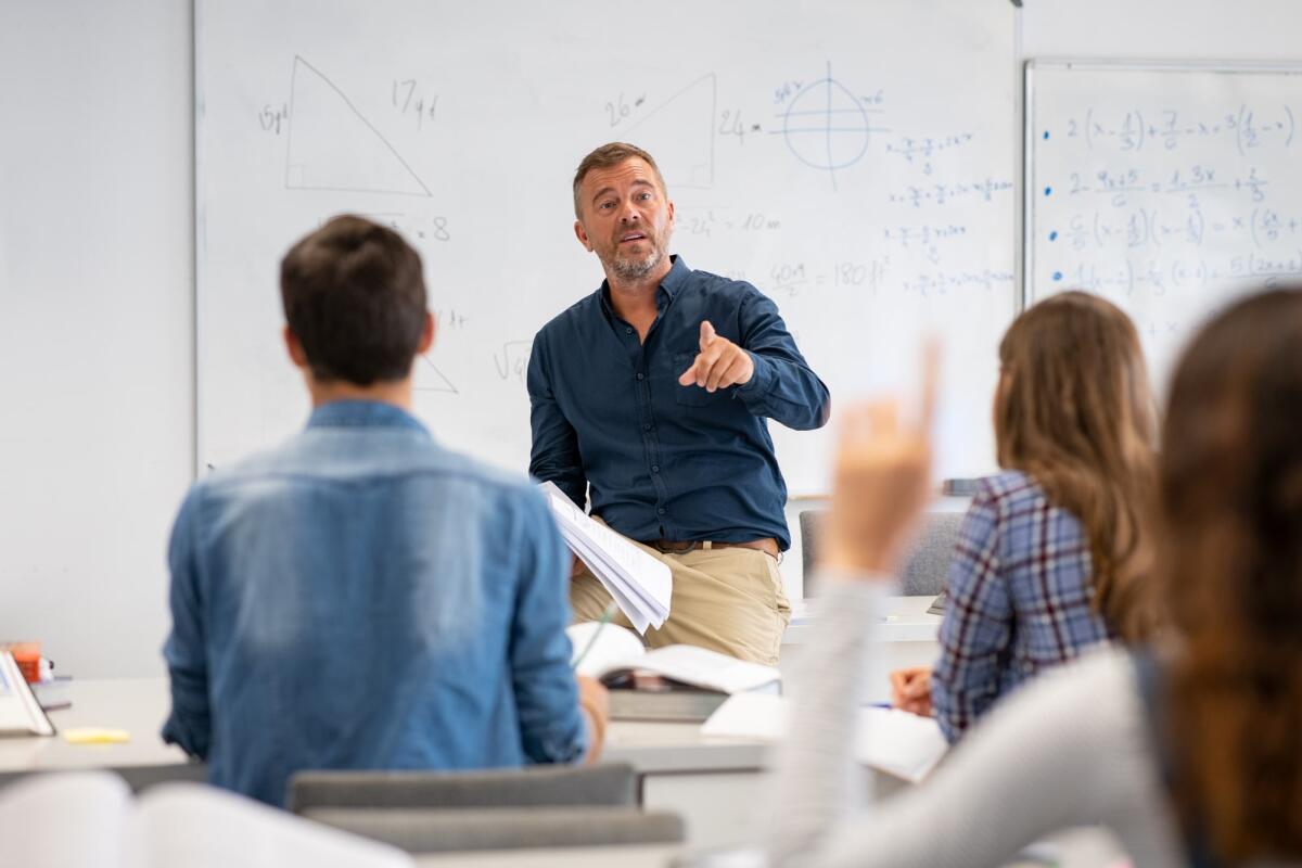 Qual è la probabilità di essere interrogati a scuola se estratti a caso? - Professor pointing at college student with hand raised in classroom. Student raising a hand with a question for the teacher. Lecturer teaching in class while girl have a question to do during a math lesson.