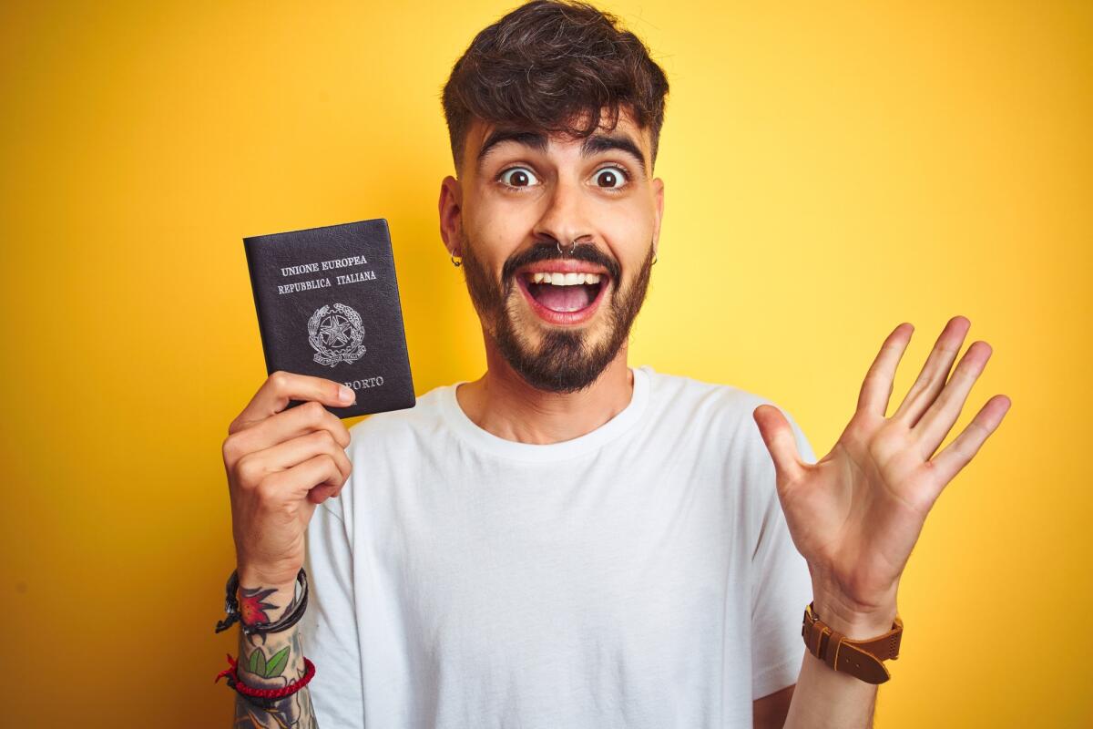 Emergenza passaporti: al via un progetto sperimentale per richiederli alle Poste - Young man with tattoo wearing Italy Italian passport over isolated yellow background very happy and excited, winner expression celebrating victory screaming with big smile and raised hands