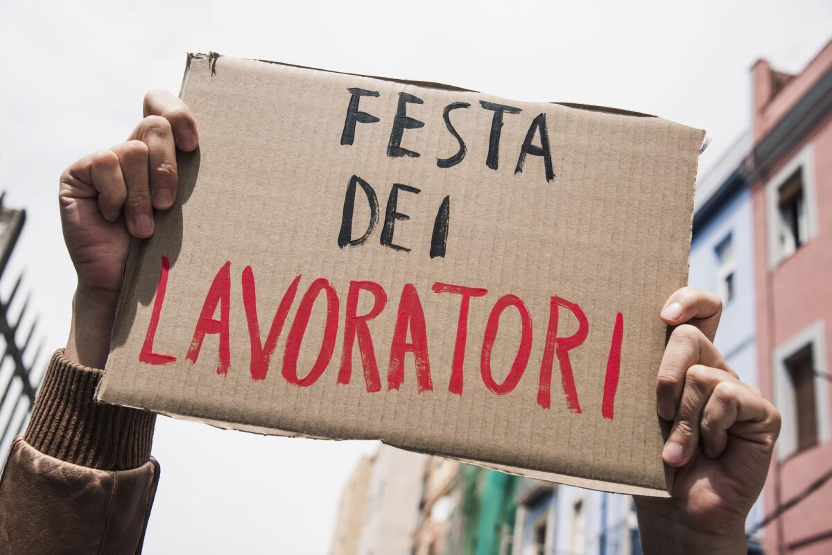 Perché il 1° maggio si celebra la Festa dei Lavoratori? - closeup of a young caucasian man outdoors showing a brown cardboard signboard with the text festa dei lavoratori, may day in italian, handwritten in it