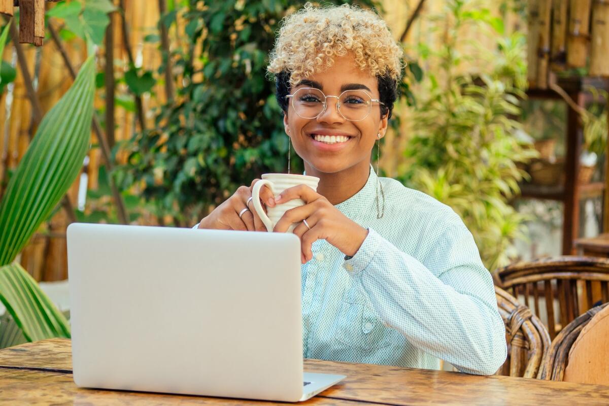 Risparmio e libera professione: ecco come ottimizzare i tuoi guadagni - african american business girl with cute curly blonde hair using laptop and have a coffee cup break at summer tropical garden cafe.