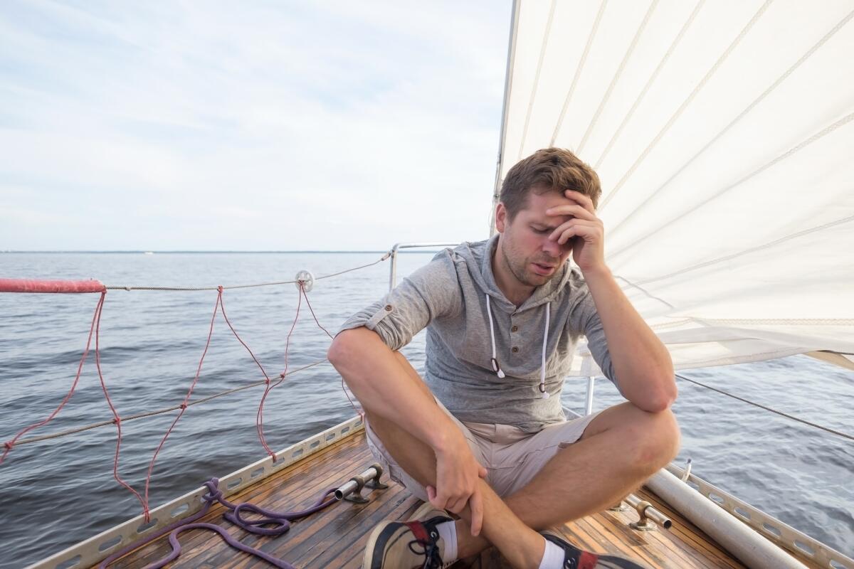 Come contrastare il mal di mare: strategie efficaci - young european man having a nausea seasickness. He is trying to stop vomiting. Travelling on old boat with sail