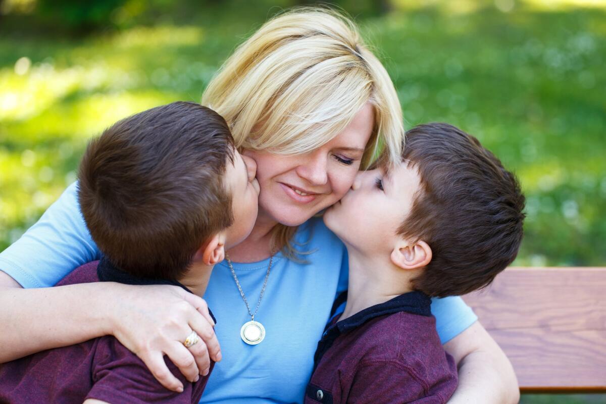 Perché la Festa della Mamma si celebra la seconda domenica di maggio? - Mother with two sons in park on bench, boys hug mom