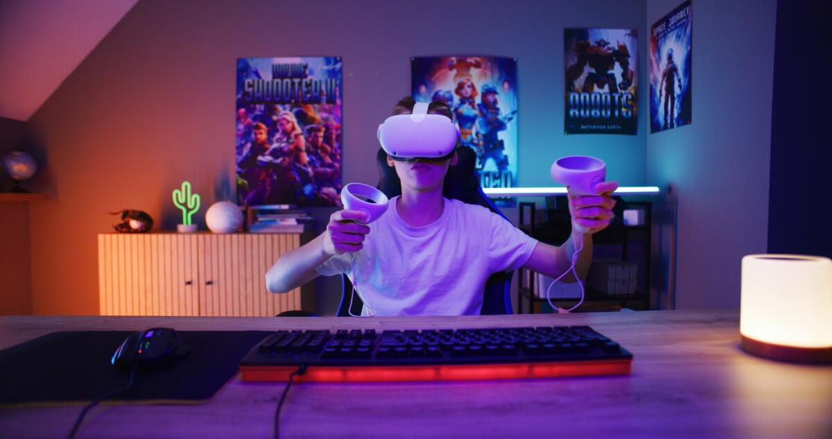 Gaming e ambiente: come creare una postazione ecosostenibile  - Young gamer in VR headset plays virtual reality online video game using wireless controllers. Boy having fun in leisure time in stylish neon room. Gaming at home. View from PC screen perspective.