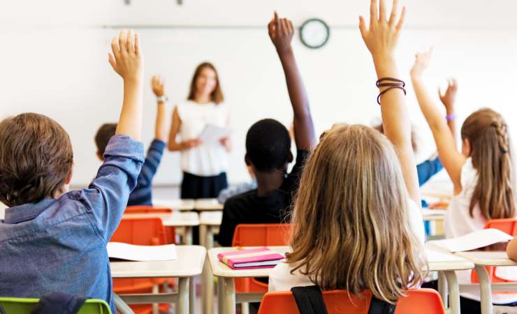 Studenti tra i banchi di scuola con la mano alzata (Canva foto) - managementcue.it