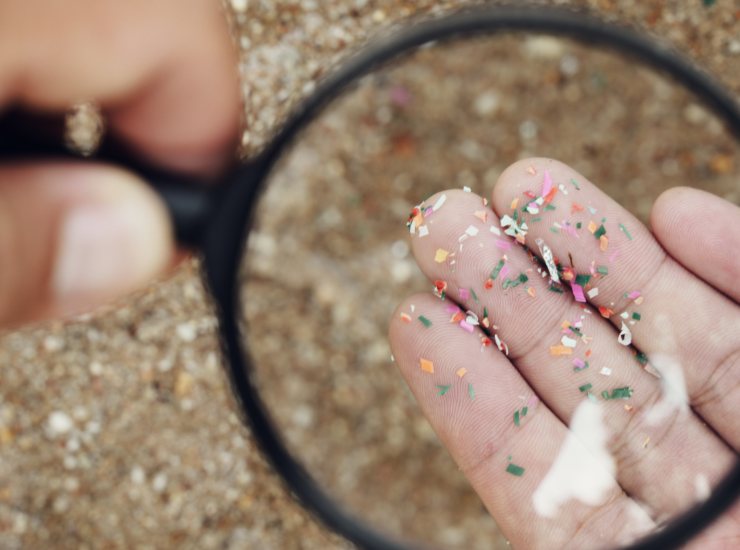 Illustrazione di alcune microplastiche sul palmo della mano (Canva FOTO) - energycue.it