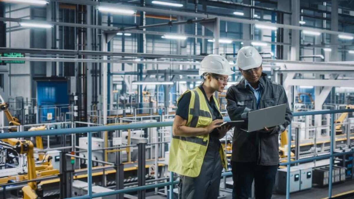 Le tecnologie che trasformano l’industria: si guarda al futuro - Male Specialist and Female Car Factory Engineer Talking and Working on Laptop and Tablet Computers. Automotive Industry 4.0 Facility Working on Vehicle Production. Diversity on Assembly Plant.